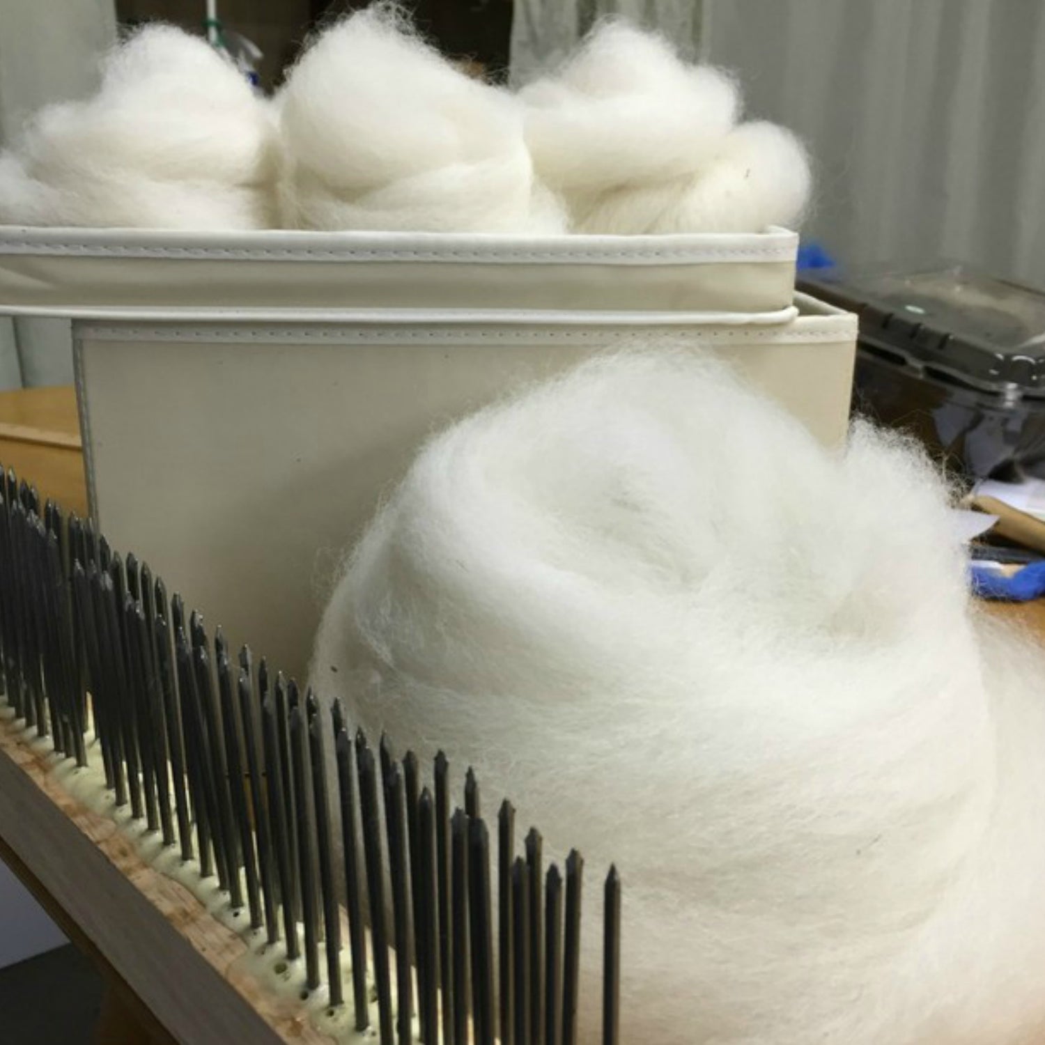 White Alpaca Roving from our beautiful alpacas sitting in a fabric box behind a fiber hackle.